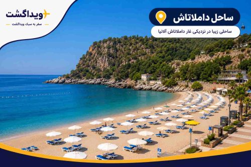 نمای ساحل داملاتاش آنتالیا با آبهای شفاف مدیترانه، ساحل شنی زیبا، چترهای ساحلی و چشمانداز کوهستانی در نزدیکی غار داملاتاش.