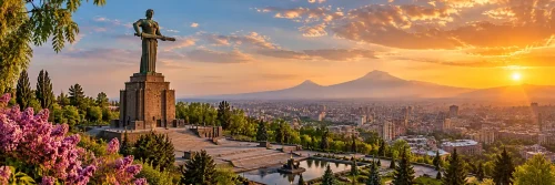 نمای پانوراما از مجسمه مادر ارمنستان در پارک پیروزی ایروان با گلهای صورتی، فضای سبز و چشمانداز شهر هنگام غروب آفتاب